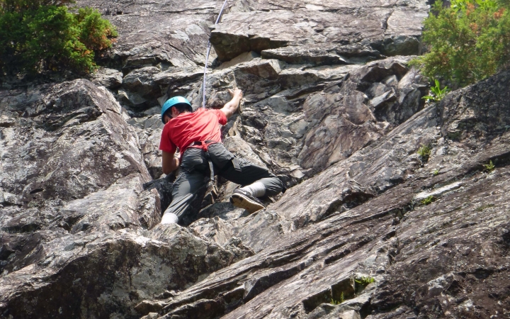 A person wearing safety gear and secured by ropes climbs a rock wall. 